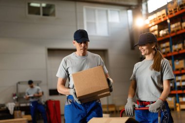 Happy woman and her male coworker working with cardboard boxes in a warehouse. 