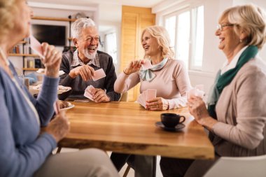 Group of mature people laughing while relaxing at home and playing cards. 
