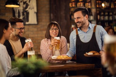 Small group of happy friends drinking beer while the waiter is serving them a snack in a tavern. 