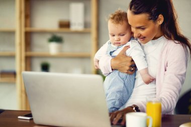 Happy mother working on a computer while being with her baby at home. 