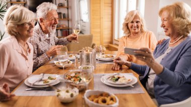Group of mature friends laughing while talking at dining table at home.
