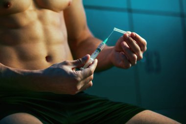 Close up of male bodybuilder about to take injection of steroids for increasing muscle growth. 