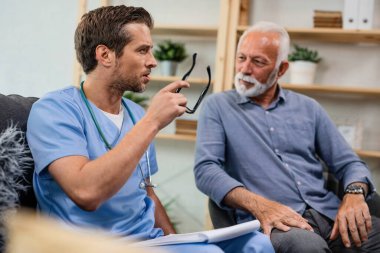 Pensive doctor with medical reports communicating with senior patient while being in a home visit. 