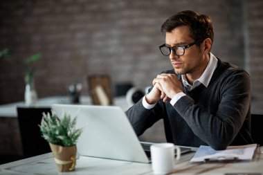 Dedicated entrepreneur sitting at office desk and reading an e-mail while working on a computer. 