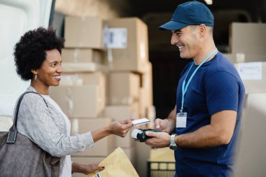 Happy African American woman using credit card while making contactless payment to a courier for package delivery. 