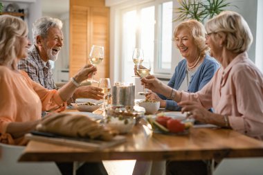 Group of happy seniors having fun while toasting with wineglasses during lunch at home. 