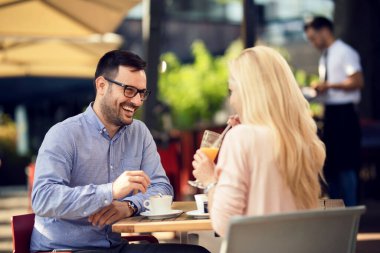 Happy man and his girlfriend talking to each other while spending time together in a cafe. 