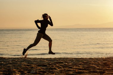 Dedicated sportswoman jogging at the beach at sunset. Copy space. 