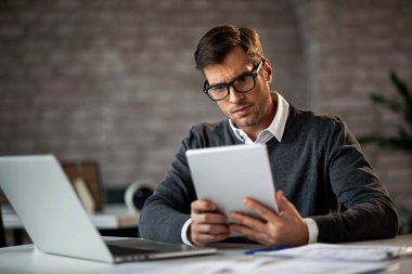 Mid adult entrepreneur working at his office desk and using digital tablet. 