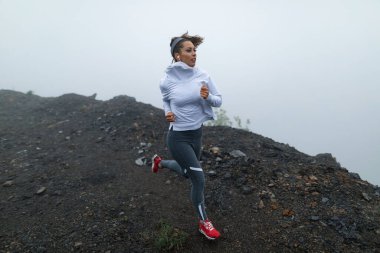 Determined female runner jogging on a cliff on cold foggy weather and listening music over earphones. Copy space. 