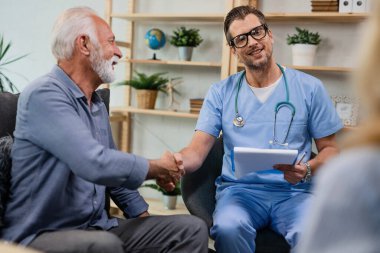 Happy doctor and senior patient handshaking after medical exam during home visit. 