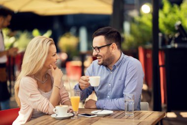 Happy couple communicating while sitting in a cafe and drinking coffee. Focus is on man. 