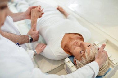 Mature woman being supported by two radiologists while undergoing for CAT scan examination at clinic. 