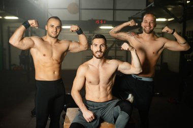 Group of muscular build men showing off with their biceps while being in a gym.