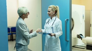 Happy female general practitioner and her mature patient greeting and shaking hands ta clinic. 