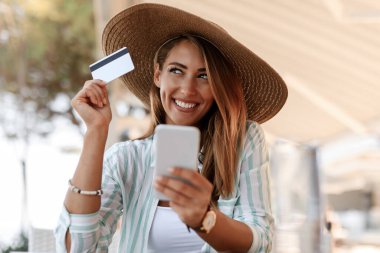 Young woman feeling satisfied while using smart phone and shopping on the Internet with credit card. 