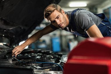 Young mechanic working on air conditioning system of a car in auto repair shop. 