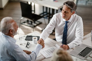Above view of happy bank manager and senior client shaking hands after successful agreement on a meeting in the office. 