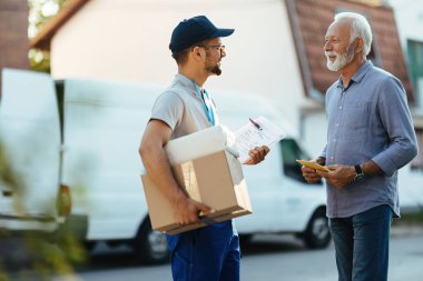 Happy mature man receiving package and communicating with young postman on the street.