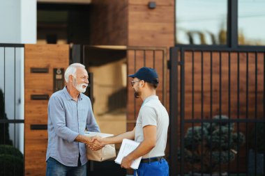 Happy senior man shaking hands with a courier while getting his package delivered. 
