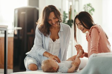 Female couple enjoying while playing with their baby boy at home. 