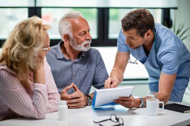 Serious doctor discussing with senior couple about their medical documents during appointment at clinic. 
