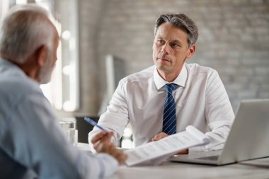 Financial advisor having a meeting with senior man and talking with him about terms of the contract in the office. 