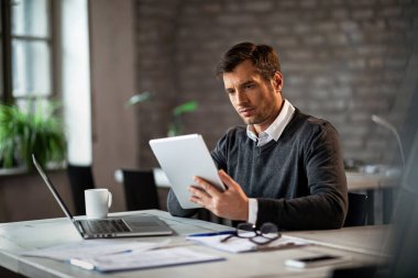 Mid adult businessman working at his desk and surfing the internet on a touchpad. 
