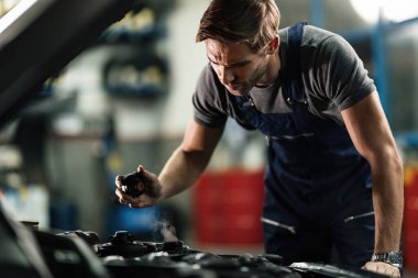 Auto mechanic opening radiator cap and checking overheated car cooling system in a workshop. 