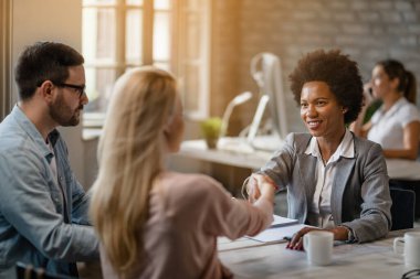 Black happy financial advisor greeting with her clients in the office. 