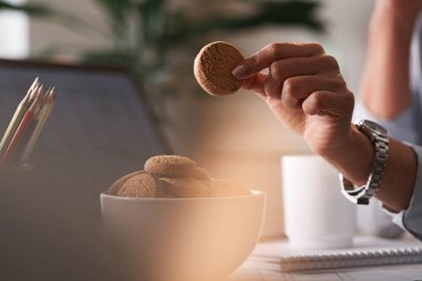 Close up of woman eating cookies while working in the office. 
