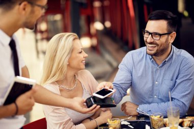 Happy couple using smart phone and making easy payment in a restaurant. 