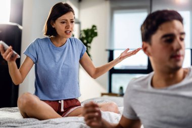 Young couple arguing in the bedroom. Focus is on frustrated woman who is in disbelief because of her boyfriend's attitude.