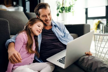 Happy father and daughter sitting embraced on the floor and watching something on laptop. 