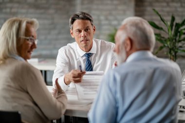 Bank manager showing to a senior couple terms of loan contract while having a meeting in the office. 