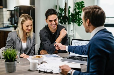 Happy couple having a meeting with real estate agent and analyzing blueprints while communicating. 