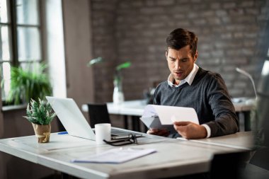 Male entrepreneur analyzing business reports while doing paperwork at his desk in the office.  