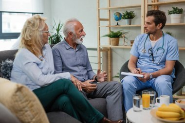 Senior man and his wife communicating about health issues with male doctor who is visiting them at home.    