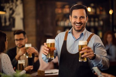 Happy waiter holding two glasses of beer and looking at camera while working in a pub. 