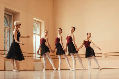 Full length of ballet teacher ad group of ballerinas rehearsing at dance studio. 