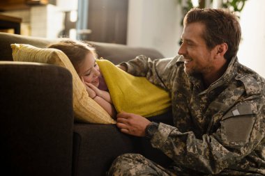 Caring military dad tucking his sleepy daughter in the living room. 