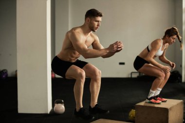 Athletic couple having cross training in health club and practicing box jumps. 