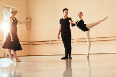 Ballet couple dancing with assistance of their instructor during ballet class in a studio. 