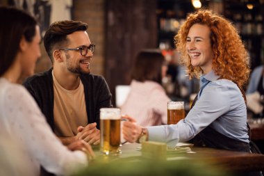Young happy waitress giving beer to a couple while serving them in a pub. 