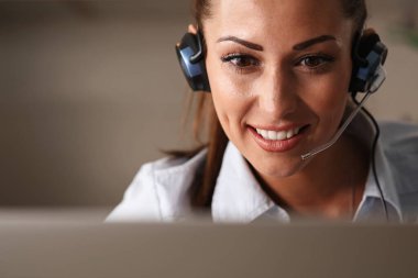 Beautiful smiling call center agent with headset communicating with a customer  over the phone. 