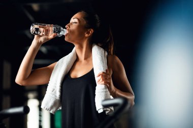 Young athletic woman refreshing herself after working out in a gym and drinking water with her eyes closed. Copy space. 