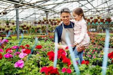 Happy father holding his small daughter while showing her flowers in a green house.