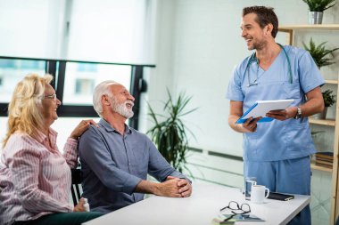 Happy mature husband and wife talking with their doctor abut their medical test results at his office. 