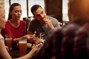 Group of young people enjoying in a pub while eating nacho chips and drinking beer in a pub. 