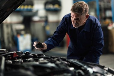 Auto mechanic opening radiator cap while repairing car in a repair workshop.